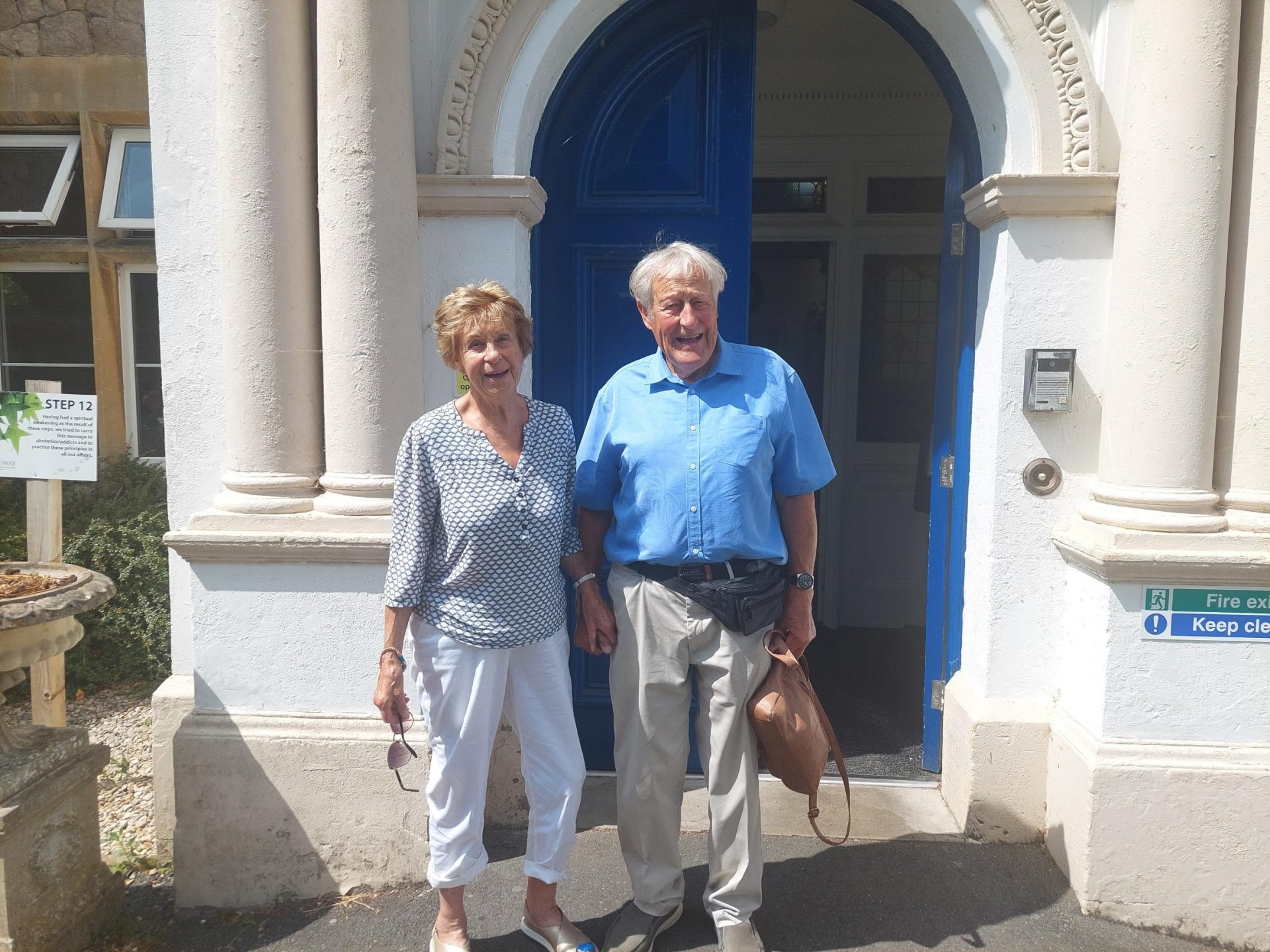 Val and John smiling outside of the Broadway Lodge front door