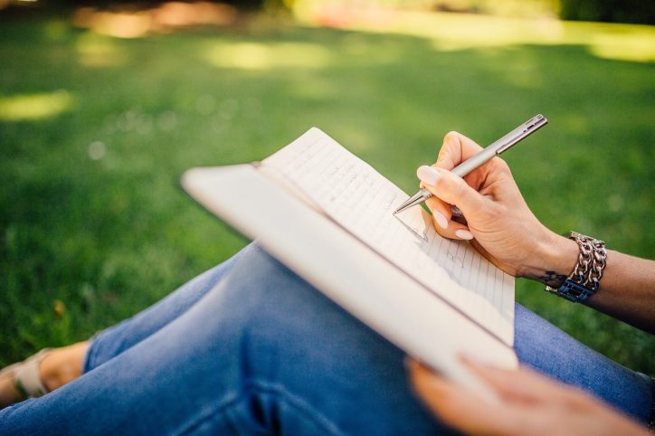 A lady writing in a notepad sat under a tree