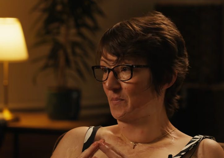 A lady sat in a darker room lit by a lamp in the background